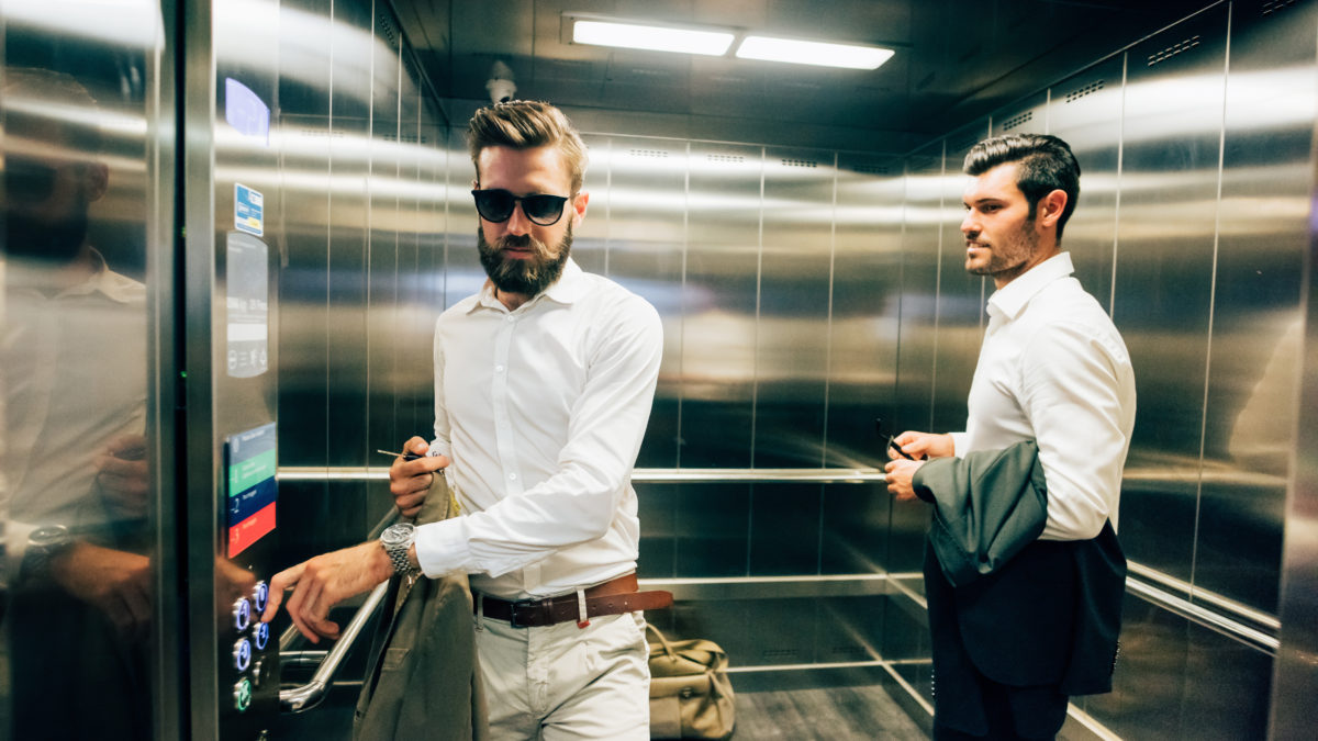 Two young handsome black and blonde hair bearded modern businessman in a elevator, one holding a bag and wearing sunglassesn- business, working, successful concept